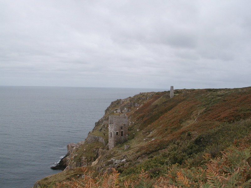 Old mining building on a gorse and fern covered hillside on a headland.