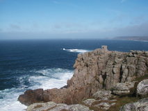 Rugged granite cliffs with tiny stone lookout building on top, sea in background