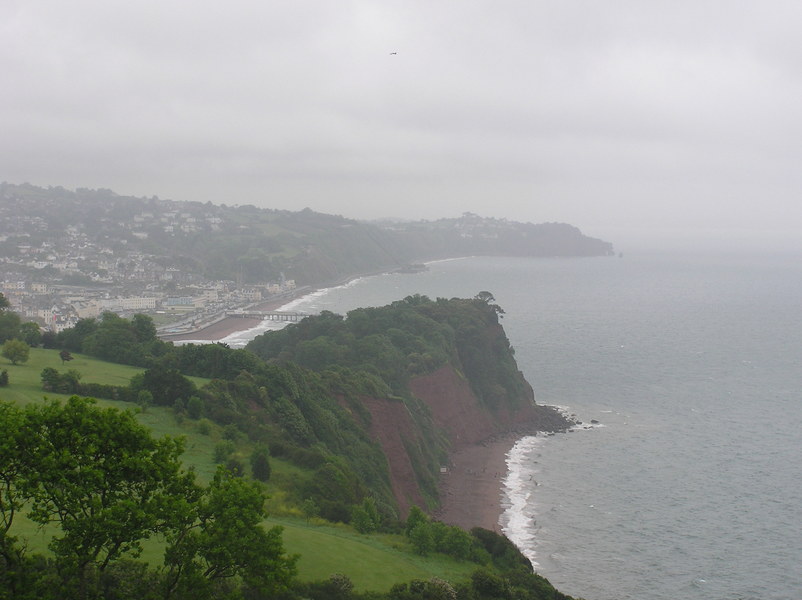 grey and drizzly view down to tree covered headland, red cliffs, and town in background.