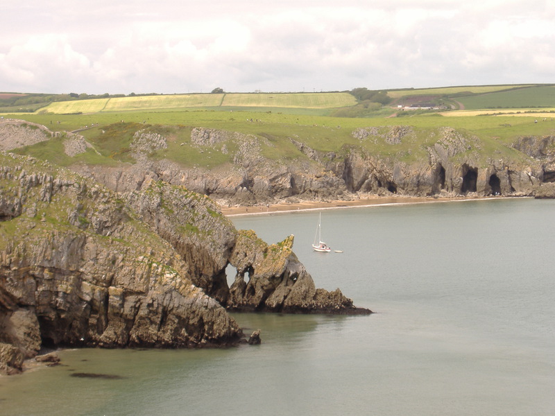 Interesting fin of rock stretching down to sea with holes in it, small bay and sailing boat in background