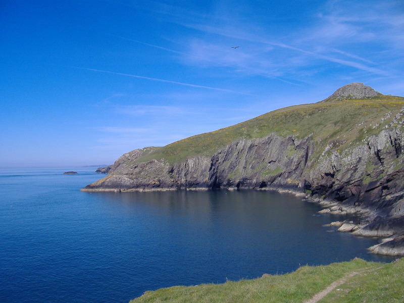 Large rock torr rising up above the sea, with steep cliffs below, clear skies