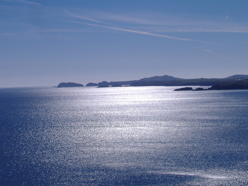 Long shot, dark headlands in the distance, sun glistening off the sea in the foreground