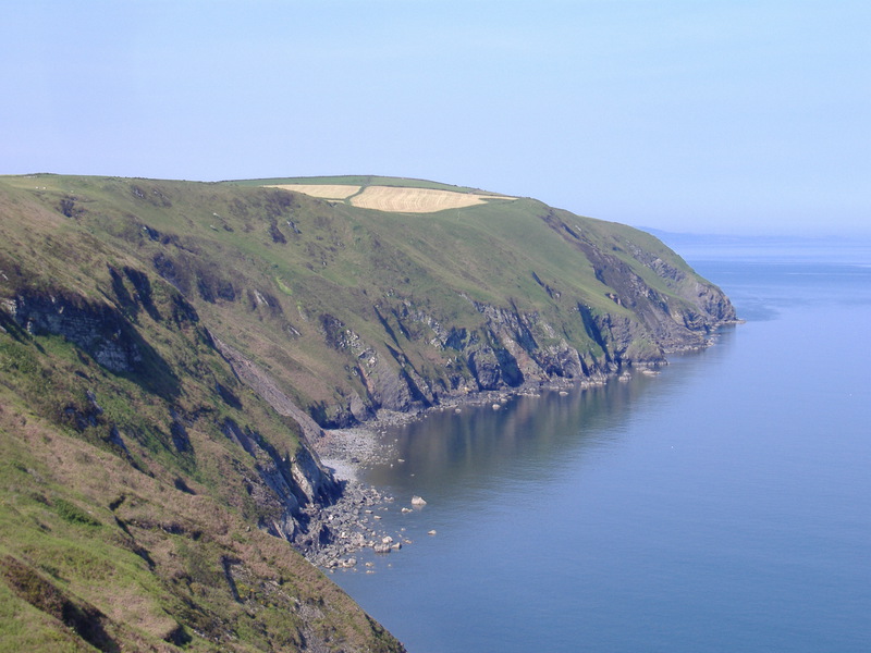 Looking back along steep cliffs and steep grassy slopes, clear blue sky
