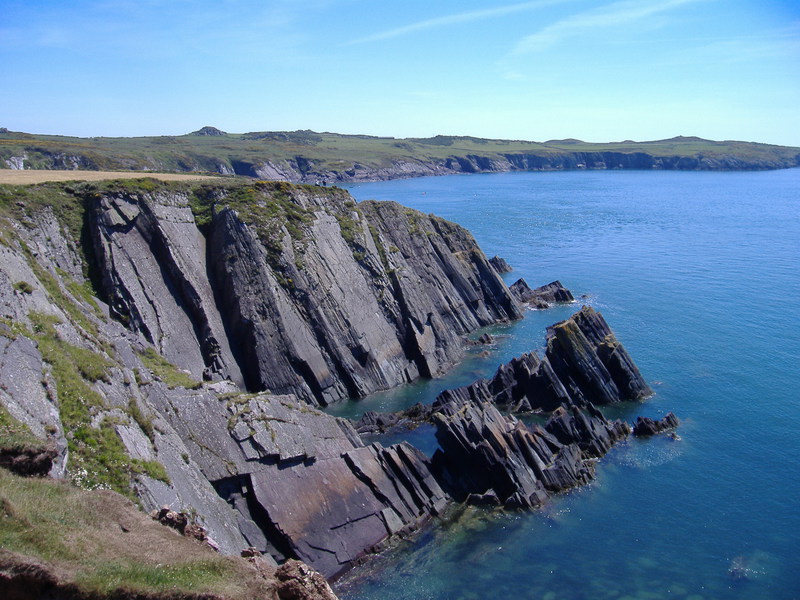 Slabs of smooth rock, angling down to the sea, small clifs along coastline stretching out in the background